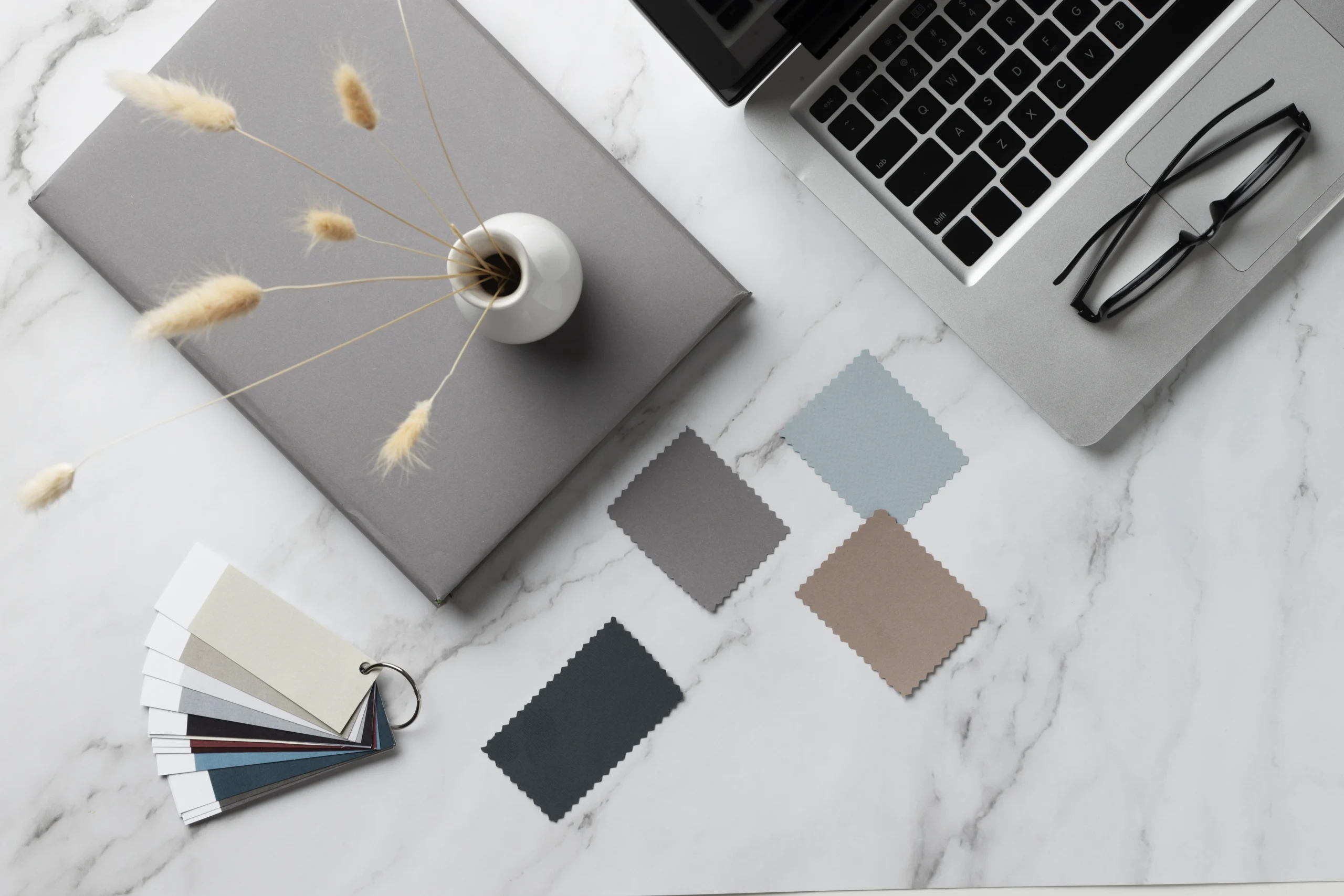 Statuario marble desk with laptop, notebook, and color and material samples for interior design workspace.