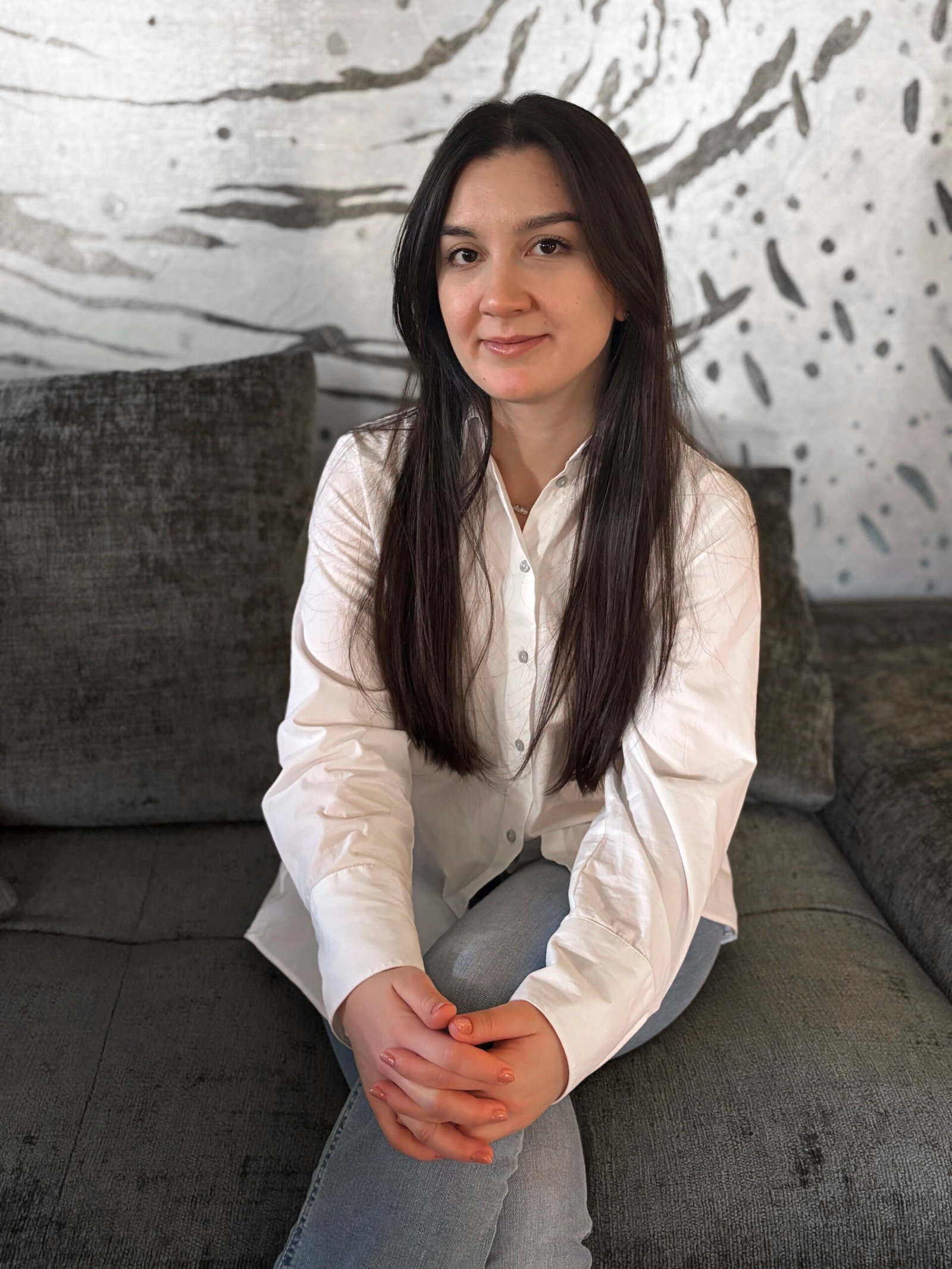 Woman sitting on a sofa in front of a wall with wallpaper in a modern interior.